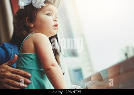 Etwas hat sie draußen aufgefallen. Eine Mutter und ihre bezaubernde kleine Tochter, die zu Hause aus dem Fenster blickten. Stockfoto