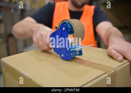 Arbeiter in einem Warenlager im Einzelhandel verpackten ein Paket mit Klebeband Stockfoto