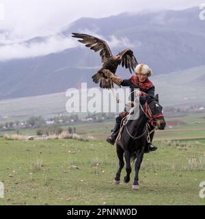 Issyk Kul, Kirgisistan - Mai 2022: Adlertrainer auf einem Pferd und seinem Goldadler, der Adler zum Jagen trainiert, mit traditionellen Techniken Stockfoto