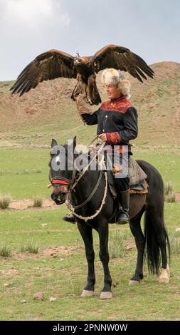 Issyk Kul, Kirgisistan - Mai 2022: Adlertrainer auf einem Pferd und seinem Goldadler, der Adler zum Jagen trainiert, mit traditionellen Techniken Stockfoto