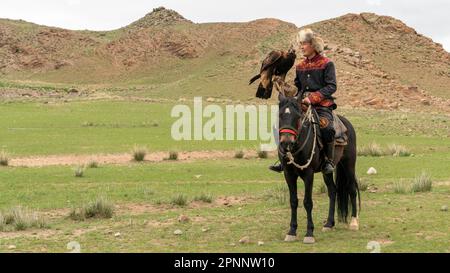 Issyk Kul, Kirgisistan - Mai 2022: Adlertrainer auf einem Pferd und seinem Goldadler, der Adler zum Jagen trainiert, mit traditionellen Techniken Stockfoto