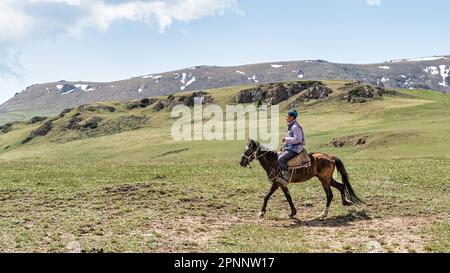 Kirgisistan - Mai 2022: Kirgisischer Mann auf dem Pferderücken in den Kirgisischen Bergen. In Kirgisistans Gebirgsregionen ist es üblich, Hirten zu beobachten Stockfoto