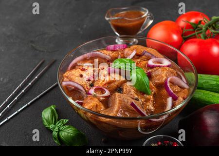 Rohes Schweinefleisch mit Kebab mariniert. Grillfleisch mit Spießen und Gemüse auf schwarzem Hintergrund. Kochen von Grillgerichten Stockfoto