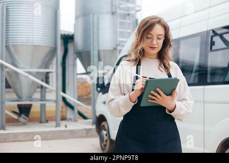 Eine Logistikerin mit Frachtbriefen steht in der Nähe eines Minibusses auf einer Produktionsfarm, Lieferung Stockfoto