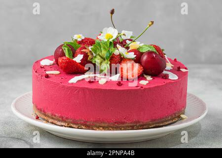 Roher veganer Erdbeeren- und Kirschkashewkuchen mit frischen Beeren, Nüssen und Blumen. Vegetarisches Dessert. Gesundes veganes Essen Stockfoto