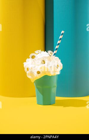 Cremiger Milchshake mit Gänseblümchen und Papierstroh auf gelbem und blauem Hintergrund. Stockfoto