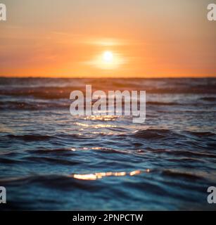 Sonnenuntergang auf dem Meer, mit dem warmen Licht, das die Wellen nahe der Küste am Ende eines Tages am Strand einfängt, mit blauen Farben des Wassers. Stockfoto