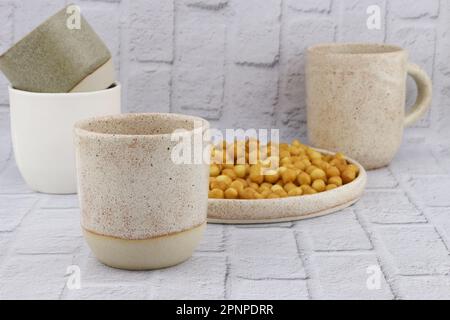 Keramikbecher in verschiedenen Größen und Farben. Glas- und Plattenset aus Keramik auf grauem Hintergrund. Steingut mit Matte Glasur überzogen. Cerami Stockfoto