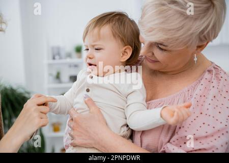 Lächelnde reife Frau umarmt verärgertes Baby Mädchen in der Küche, Bild der Börse Stockfoto