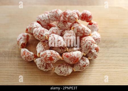 Mini-Salami auf einem Holzbrett. Trocken gepökelte Portionswurst-Cabanossi in weißer Verpackung. Würstchen in einer natürlichen Hülle aus Hühnchen- und Schweinefleisch. Stockfoto