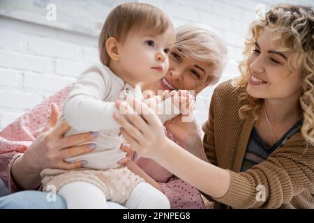 Ein kleines Mädchen, das fast wegschaut, glückliche Mutter und Oma im Wohnzimmer, Stock Image Stockfoto