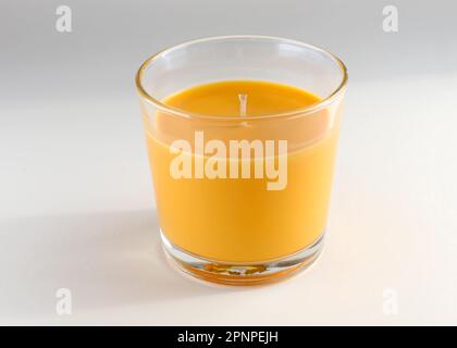 Orangefarbene Duftkerze im Glashalter auf dem Tisch. Paraffinkerze in einem durchsichtigen Glas für zu Hause. Eine Kerze mit Orangenduft in Nahaufnahme. Stockfoto