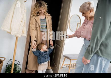 Glückliche Frau mittleren Alters, die die Tür zur Tochter öffnet, mit einem kleinen Mädchen zu Hause, Stock Image Stockfoto