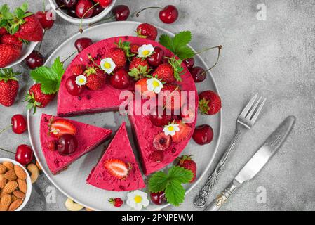 Roher, veganer Erdbeeren- und Kirschkashewkuchen mit frischen Beeren, Nüssen und Blumen. Vegetarisches Dessert. Draufsicht. Gesundes veganes Essen Stockfoto