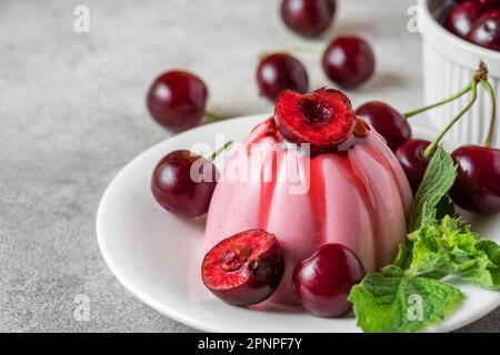 Köstliches Cherry-Panna-Cotta-Dessert mit frischen Kirschbeeren, Fruchtsauce und Minze auf einem Teller auf einem grauen Tisch. Italienisches Essen. Stockfoto