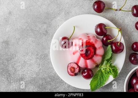 Italienisches Dessert. Cherry Panna Cotta mit frischen Beeren, Fruchtsauce und Minze auf grauem Hintergrund. Draufsicht mit Kopierbereich Stockfoto