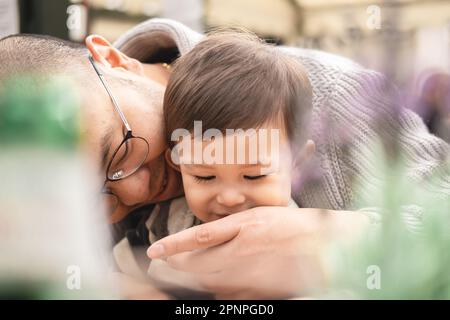 Traumhaftes Bild von Vater und Sohn, männliches Kind, das auf den Beinen seines Vaters sitzt und Gläser im Biergarten im Pub in Edinburgh trägt. Intimer, fürsorglicher Moment. Stockfoto