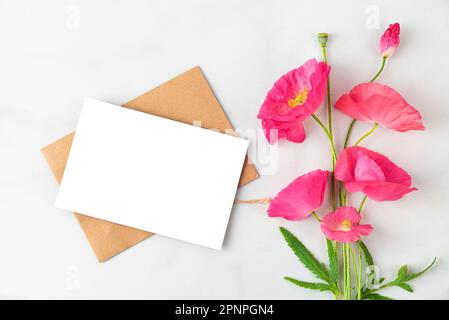 Unbeschriftete Grußkarte mit pinkfarbenem Mohnblumenstrauß auf weißem Hintergrund. Hochzeitseinladung. Modell. Flach verlegt. Draufsicht Stockfoto