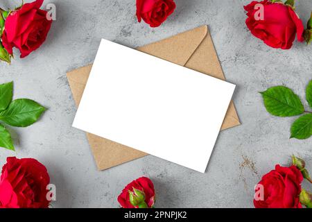 Leere Grußkarte im Rahmen aus roten Rosenblumen auf grauem Hintergrund. Hochzeitseinladung. Modell. Flach verlegt. Grundriss Muttertag, Valentinstag Stockfoto