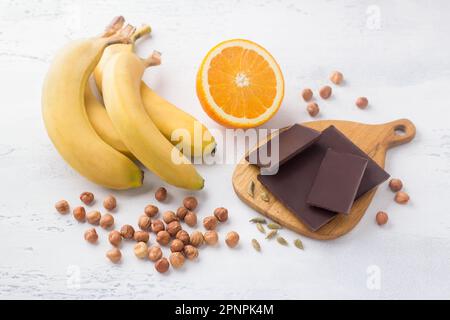 Bananen, Orange, Schokolade, Nüsse und Kardamom auf hellblauem Hintergrund. Zutaten für ein veganes Dessert. Köstliches hausgemachtes Essen Stockfoto