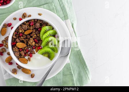 Gesundes Frühstück. Schüssel mit Schokoladenhafer, hausgemachtem Müsli mit frischem Obst und Beeren auf Serviette mit einem Löffel auf weißem Hintergrund. Draufsicht Stockfoto