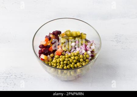 Glasschüssel mit Vinaigrettensalat aus Gemüse, Rüben, Karotten, Kartoffeln, grünen Erbsen in Dosen und roten Zwiebeln auf hellblauem Hintergrund. Homema kochen Stockfoto