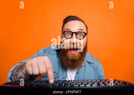 Großaufnahme eines lustigen Geschäftsmanns Probieren Sie sein erstes E-Commerce-Produkt. Tragen Sie eine Tastatur mit Brille, die auf einem orangefarbenen Hintergrund isoliert ist Stockfoto