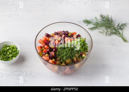 Glasschüssel mit Vinaigrettensalat aus Gemüse, Rüben, Karotten, Kartoffeln, grünen Erbsen in Dosen und roten Zwiebeln auf hellblauem Hintergrund. Homema kochen Stockfoto