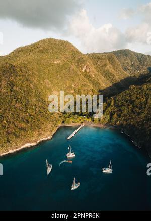 Panoramafoto der Drohne Anse d'arlet in Martinique, Karibikinsel, mit Segelbooten, türkisfarbenem Wasser und wolkenblauem Himmel im Hintergrund. Stockfoto