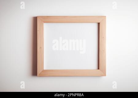 Heller Bilderrahmen aus Holz mit quadratischer Form, der an einem weißen Wandmodell für Bilder und Poster hängt Stockfoto