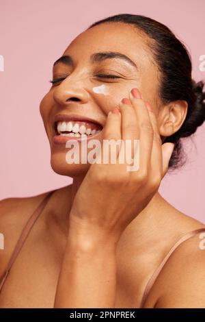 Nahaufnahme einer schönen Frau, die Feuchtigkeitscreme auf ihr Gesicht aufträgt. Frau mit Anti-Aging-Creme und Lächeln. Stockfoto