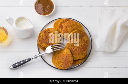 Gesunde Kürbis-Pfannkuchen mit Haferflocken serviert mit Honig und Sahne auf weißem Hintergrund. Leckeres vegetarisches Essen Stockfoto