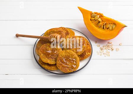 Gesunde Kürbis-Pfannkuchen mit Haferflocken mit Honig auf weißem Hintergrund. Leckeres vegetarisches Essen Stockfoto