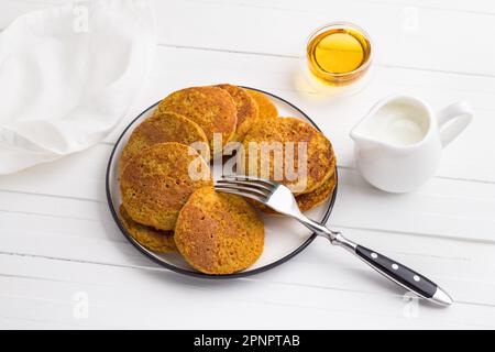 Gesunde Kürbis-Pfannkuchen mit Haferflocken serviert mit Honig und Sahne auf weißem Hintergrund. Leckeres vegetarisches Essen Stockfoto