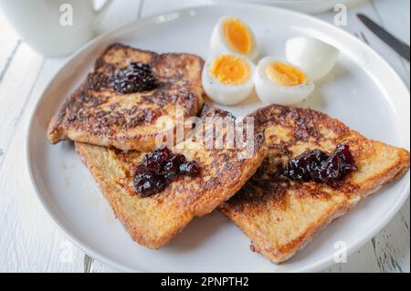 Französischer Toast mit Heidelbeermarmelade und gekochten Eiern auf einem Teller zum Frühstück Stockfoto