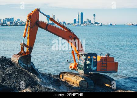 Bagger oder Bagger arbeiten an Erdbewegungsarbeiten in Landschutzarbeiten in Batumi. Orangefarbener Baggerlader gräbt Sand und Kies in Steinbrüchen. Bagger während der Aushubarbeiten Stockfoto