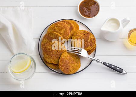 Gesunde Kürbis-Pfannkuchen mit Haferflocken serviert mit Honig und Sahne auf weißem Hintergrund. Leckeres vegetarisches Essen Stockfoto