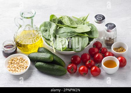 Zutaten für Salat: Spinat, Kirschtomaten, Gurken, Pinienkerne, Olivenöl, Senf, Honig, Balsamico-Essig, Salz und schwarzer Pfeffer auf einem g. Stockfoto