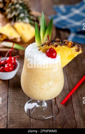 Pina-Colada-Cocktail mit Kirsche, Ananasscheiben und Blättern auf einem rustikalen Holztisch Stockfoto