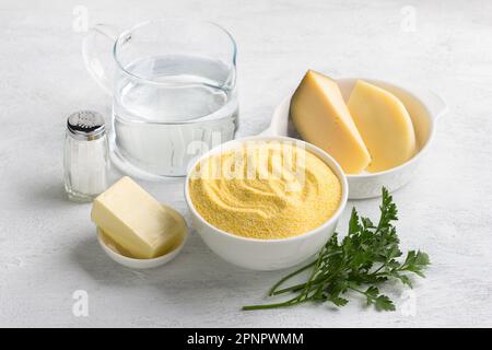 Zutaten für die Zubereitung von italienischer Polenta mit Käse: Maisgrütze, zwei Käsesorten, Butter, Salz und Wasser. Köstliches hausgemachtes vegetarisches Foo Stockfoto