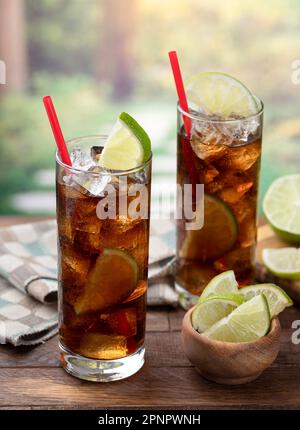 Rum-Cola-Cocktail mit Limettenscheiben auf einem rustikalen Holztisch mit Sommerhintergrund und Kopierbereich Stockfoto