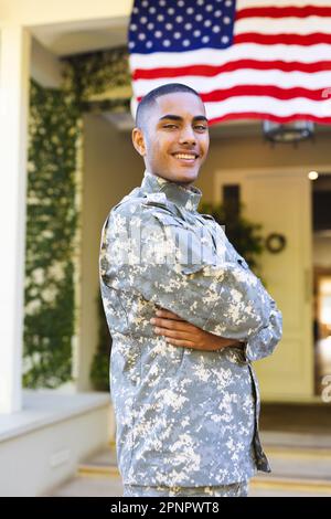 Porträt eines glücklichen, birassischen, männlichen amerikanischen Soldaten in Militäruniform, der vor dem Haus steht Stockfoto