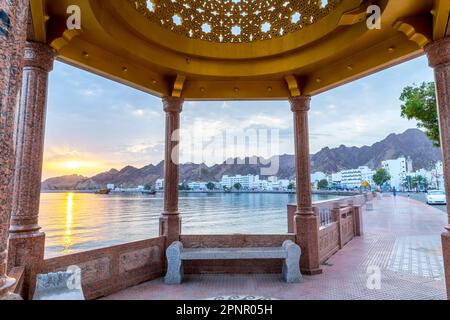 Gebäude entlang der Uferpromenade mit Bergkulisse bei Sonnenaufgang, Muscat, Oman Stockfoto