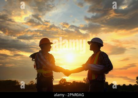 Silhouette von zwei Ingenieuren auf einer Baustelle, die bei Sonnenuntergang in Thailand die Hand schütteln Stockfoto