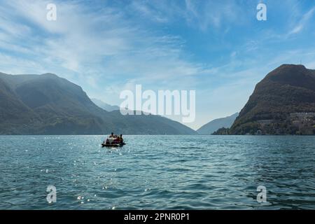 Entfernte Rückansicht von zwei Frauen, die in einem Paddelboot segeln, Luganer See, Schweiz Stockfoto