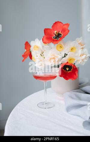 Nahaufnahme eines Cocktails auf einem Tisch neben einer Vase aus Tulpen und Narzissen Stockfoto