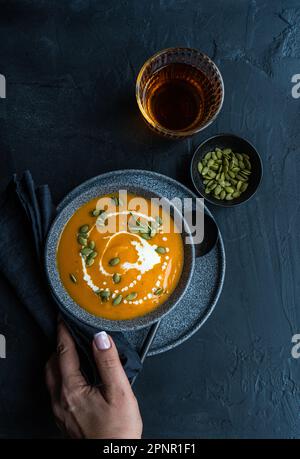 Blick von oben auf eine Frau, die nach einer Schüssel Kürbissuppe mit saurer Sahne und einem Glas Wein greift Stockfoto