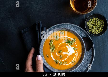 Blick von oben auf eine Frau, die nach einer Schüssel Kürbissuppe mit saurer Sahne und einem Glas Wein greift Stockfoto