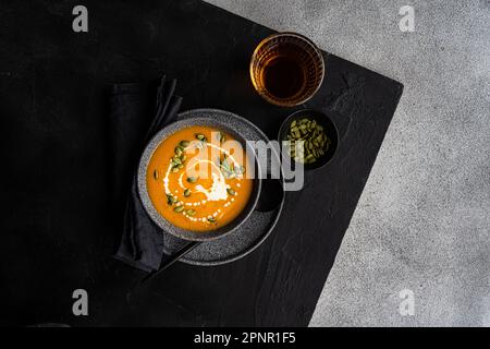 Blick von oben auf eine Schüssel Kürbissuppe mit saurer Sahne, Kürbiskernen und einem Glas Wein Stockfoto