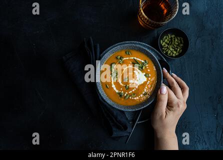 Blick von oben auf eine Frau, die nach einer Schüssel Kürbissuppe mit saurer Sahne und einem Glas Wein greift Stockfoto